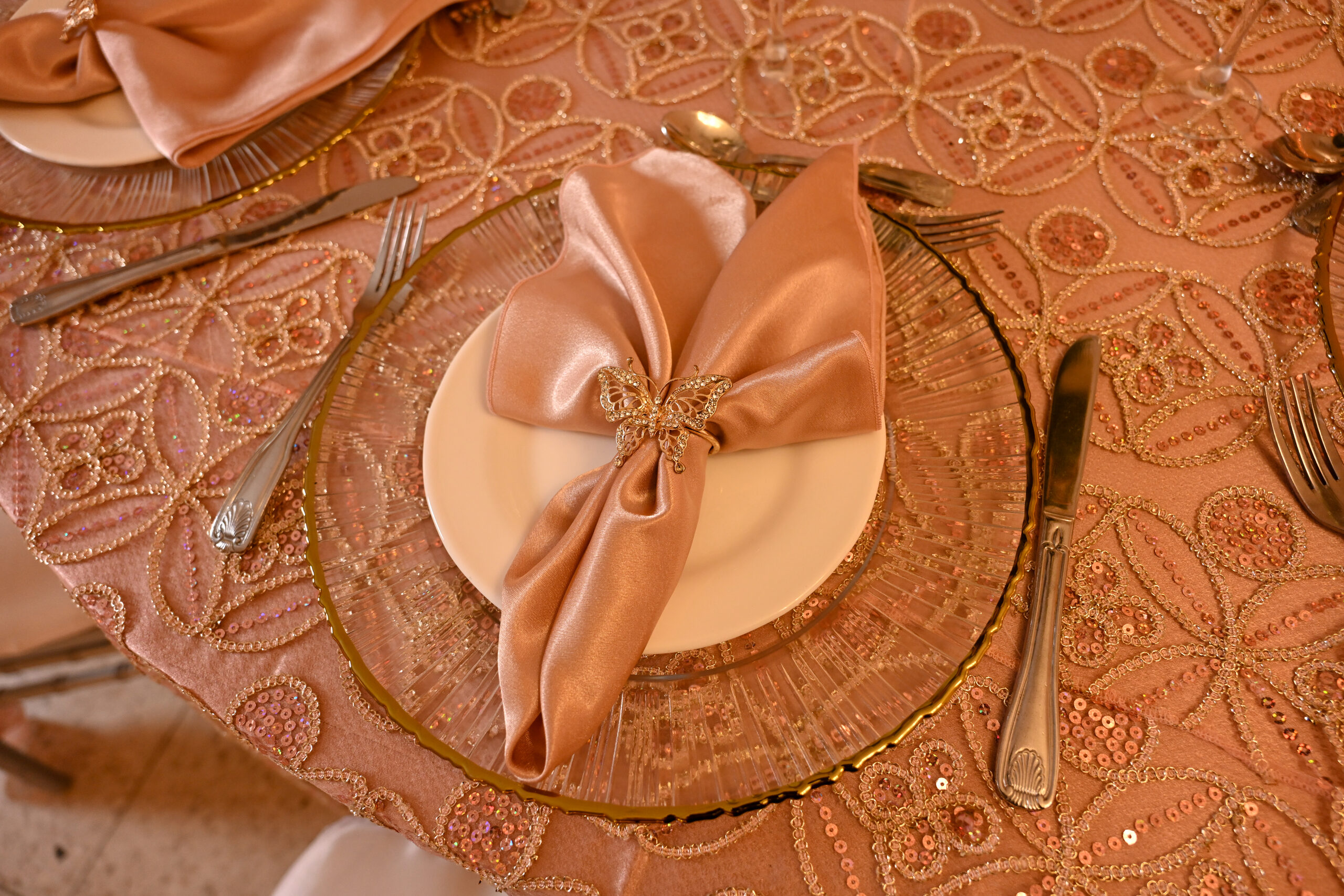 A place setting with a gold-rimmed charger and folded satin napkin