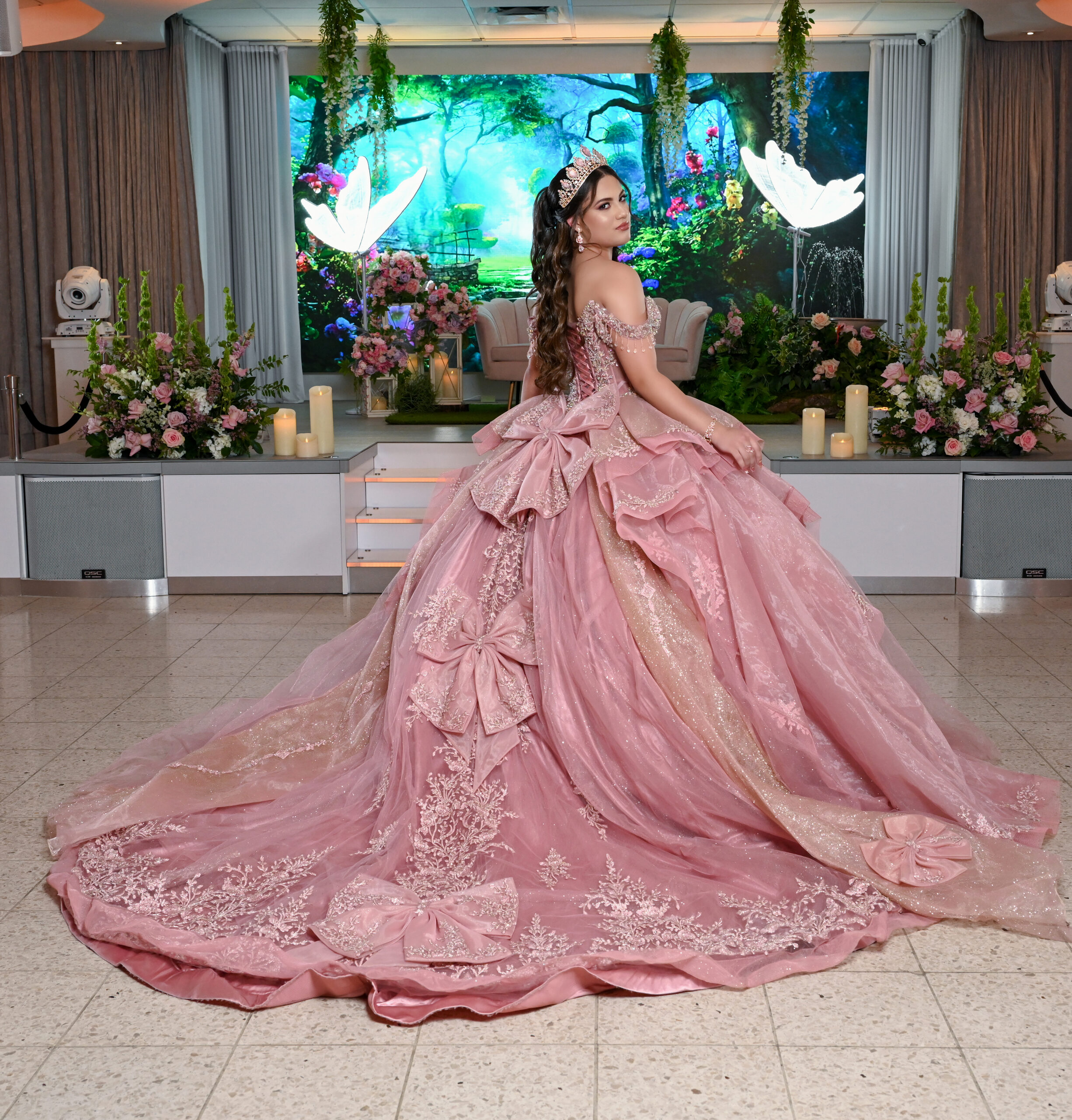 A quinceañera in a blush gown on the lit stage